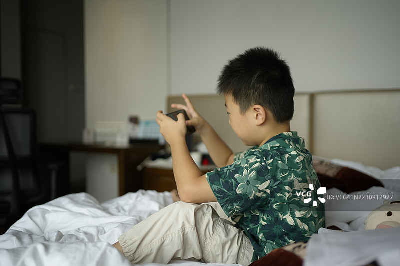 一个小男孩坐在床上玩视频游戏图片素材