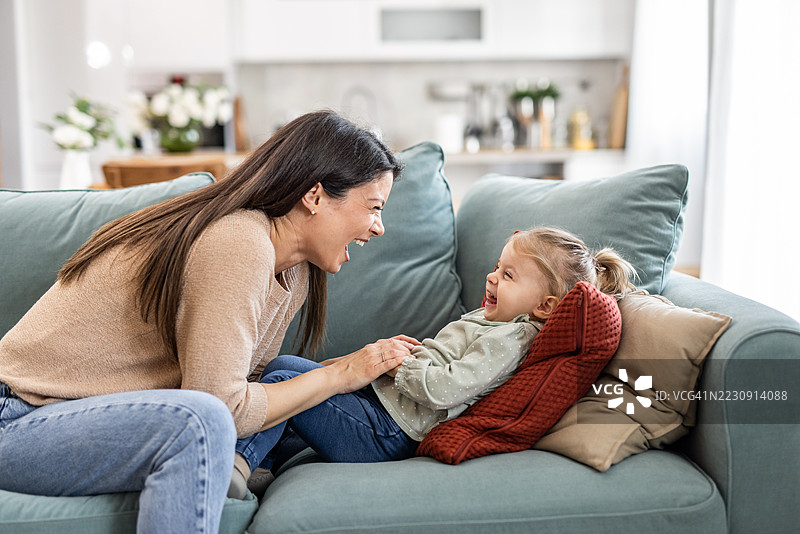 母亲在沙发上挠女儿，享受在家里的快乐时光图片素材