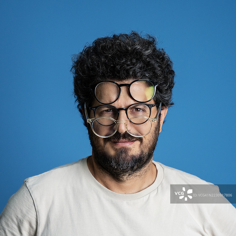 一位留着胡子的男子在工作室肖像中，脸上叠戴着几副眼镜。图片素材