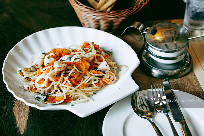海鲜意大利面配番茄酱、大蒜和香草，盛放在白盘中。意大利美食，海鲜意面和餐饮摆盘概念。图片素材