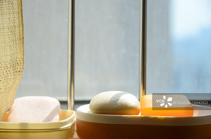 早晨的阳光照射在浴室肥皂上。自然光透过浴室窗户洒在窗台上的手工肥皂上，斜射的阳光形成柔和的阴影，突显了肥皂的纹理表面。图片素材