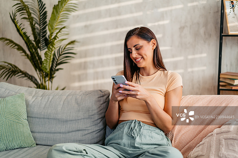 年轻女性坐在家里的沙发上发短信图片素材