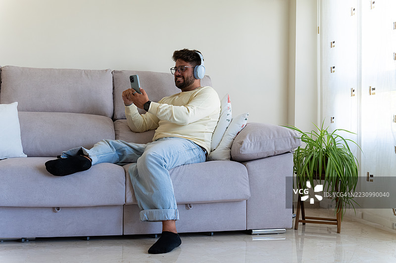 年轻男子在沙发上放松，享受音乐和社交媒体图片素材