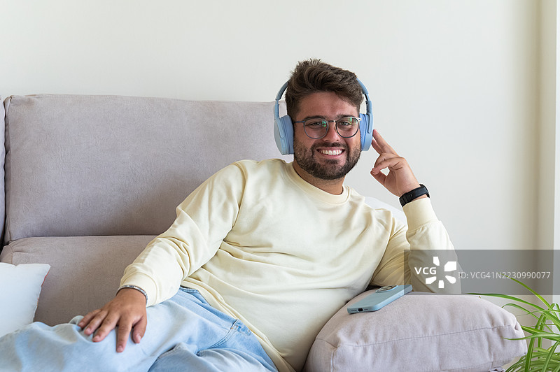 年轻男子在家中戴着耳机放松地坐在沙发上听音乐图片素材