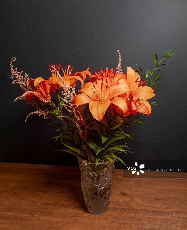装饰性花瓶中的鲜艳橙色百合放在木桌上图片素材