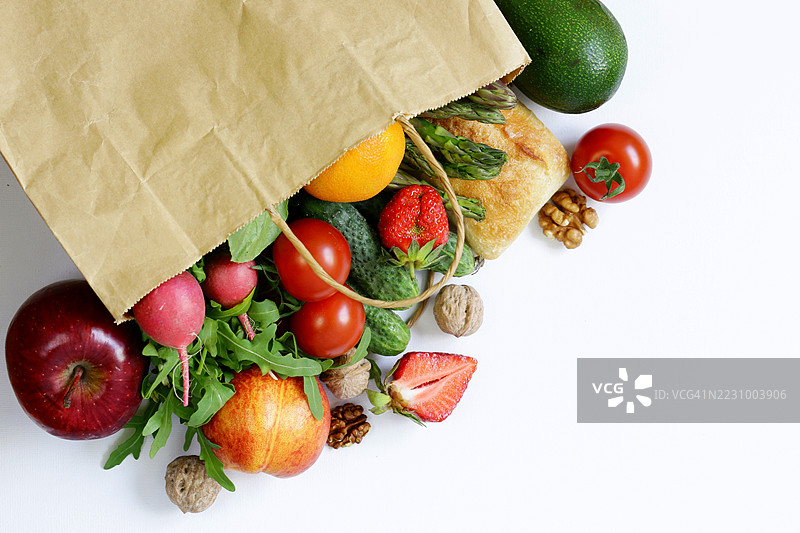 新鲜水果和蔬菜从纸袋中洒落在白色背景上图片素材