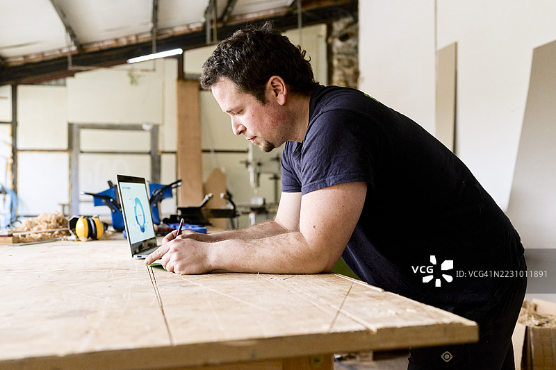 木匠在工作坊使用笔记本电脑设计家具图片素材