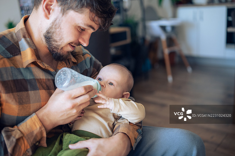 关心的年轻父亲正在用奶瓶喂他的婴儿儿子。图片素材