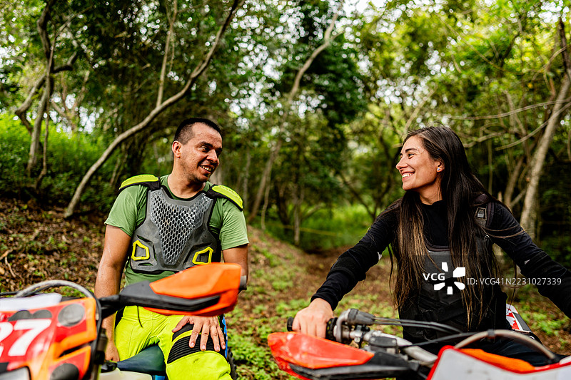 一对情侣在森林中骑越野摩托车，骑行时交谈。图片素材