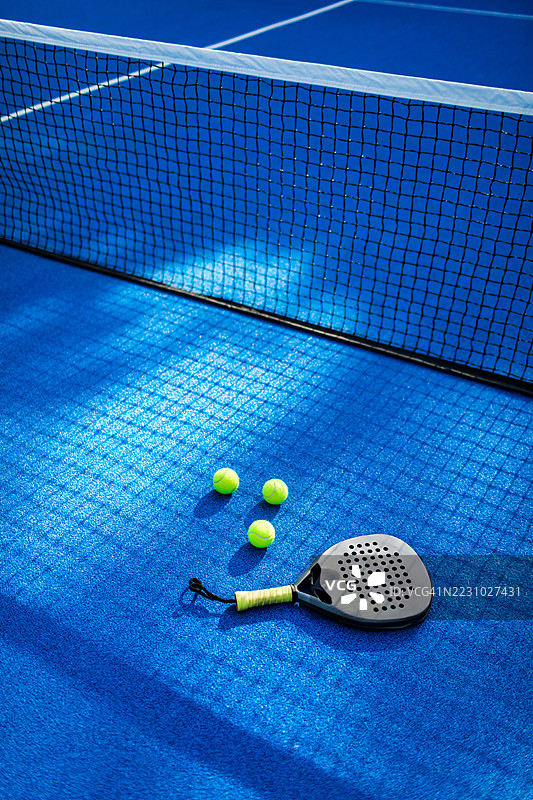 蓝色场地上的壁球拍和球，阳光明媚，网子清晰可见图片素材