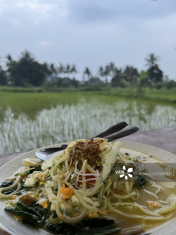 传统的爪哇炒面汤，配有鸡蛋和蔬菜，旁边是稻田图片素材