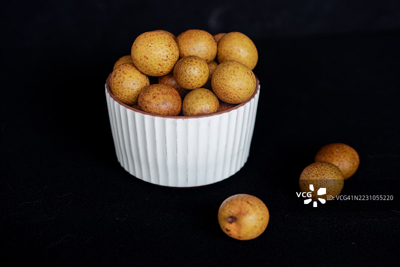 白色陶瓷碗里装满了新鲜的龙眼果，桌子上还散落着一些。图片素材