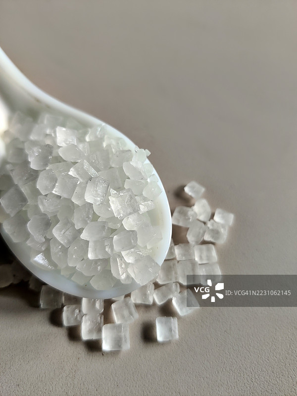 白色背景下的白色陶瓷勺中盛放着岩石糖/晶体糖果/蜜饯静物图图片素材