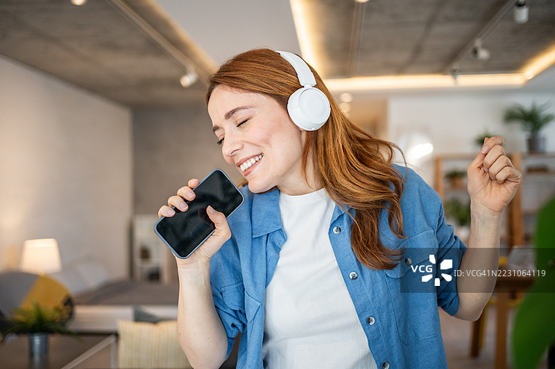 年轻女性在家中戴着耳机和智能手机唱歌跳舞图片素材