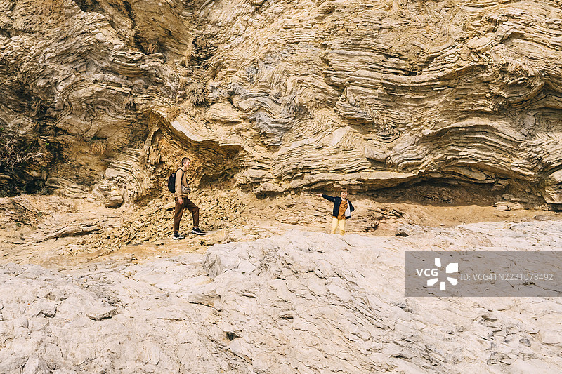 年轻父亲背着背包，带着小男孩在岩石海滩上散步。图片素材