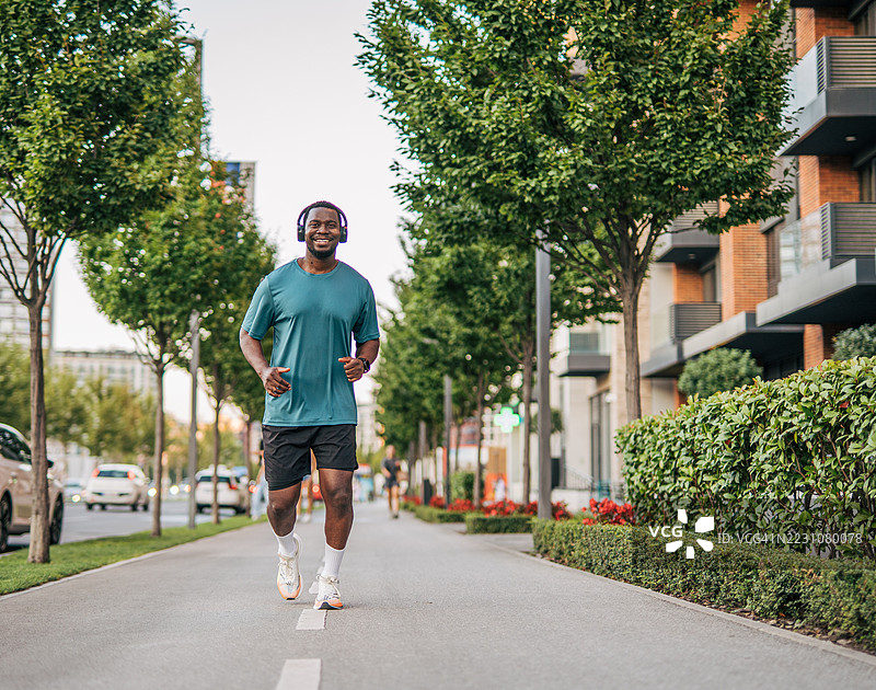 年轻男子在城市中慢跑，戴着耳机，面带微笑图片素材