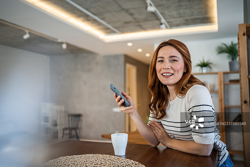 微笑的女性在家中使用智能手机放松。图片素材