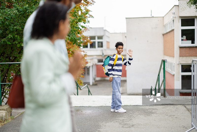小学生男孩在学校向父母挥手告别图片素材