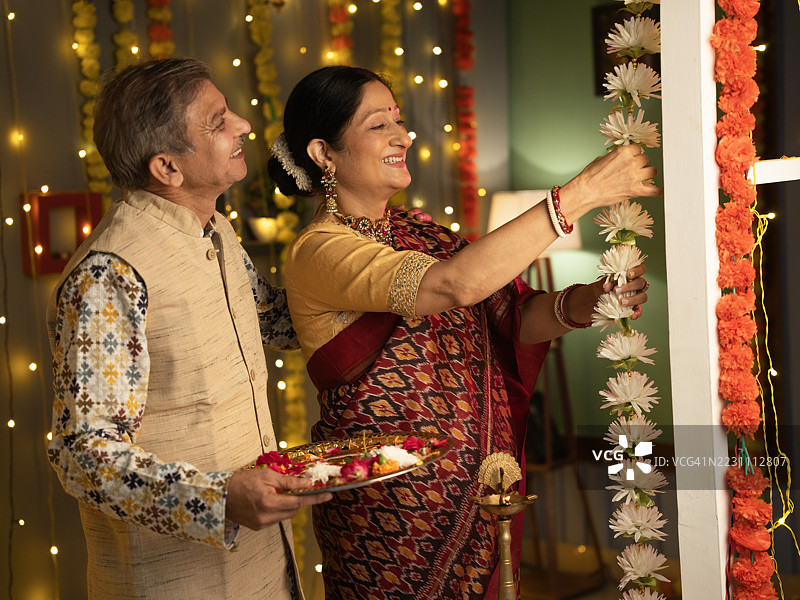 老年夫妇在排灯节期间用花环装饰房子图片素材