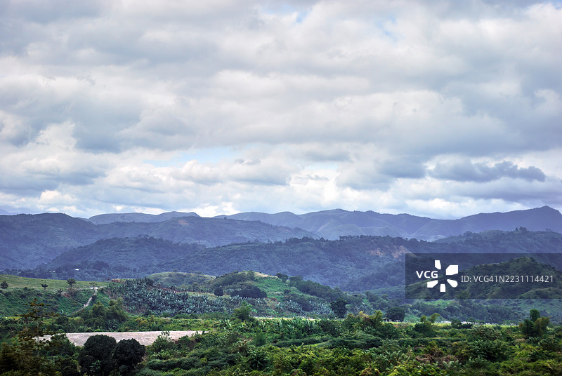层叠的山丘和山脉在多云的天空下形成的全景风景。图片素材