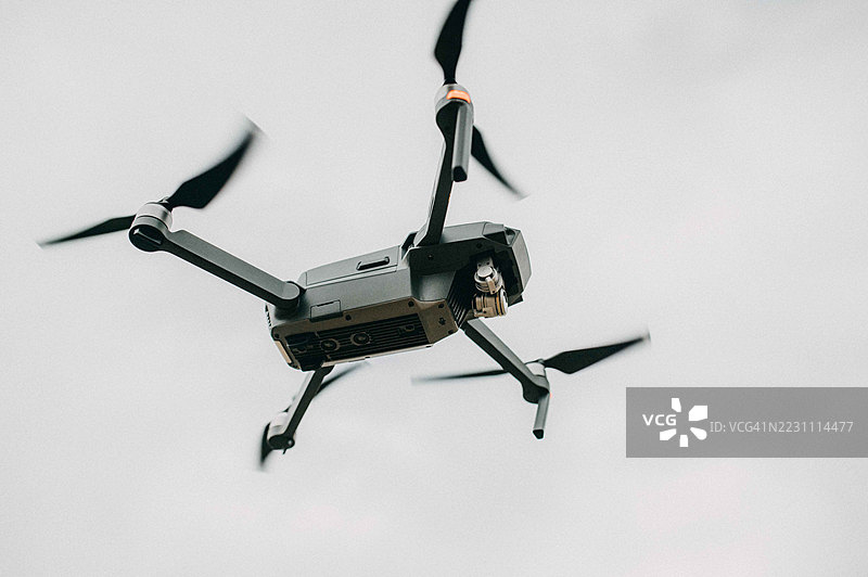 无人机在多云的天空中悬停，展示了其从高空导航和勘测地形的能力。图片素材