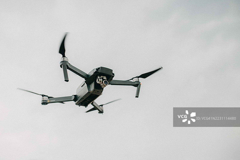 无人机在多云的天空中悬停，展示了其从高空导航和勘测地形的能力。图片素材