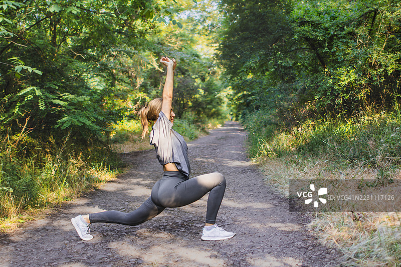 美丽的年轻女性穿着运动服，在大自然中热身或拉伸。她在锻炼过程中平衡力量与柔韧性。积极的生活方式、心理健康与健身。图片素材
