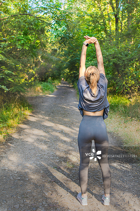 美丽的年轻女性穿着运动服，在大自然中热身或拉伸。她在锻炼过程中平衡力量与柔韧性。积极的生活方式、心理健康与健身。图片素材
