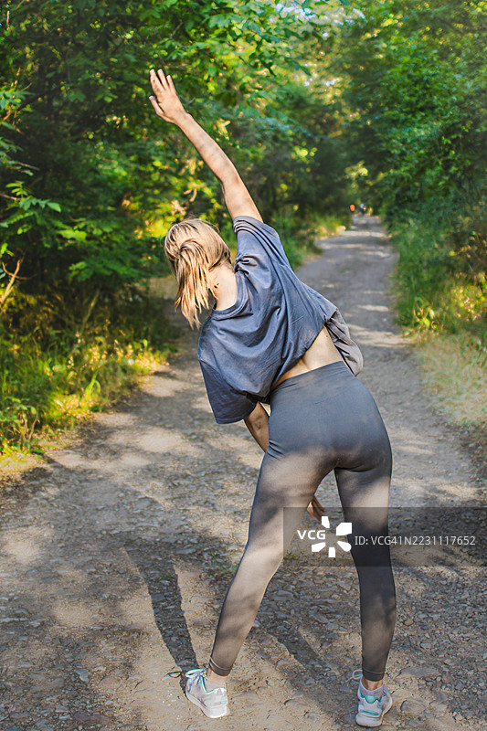 美丽的年轻女性穿着运动服，在大自然中热身或拉伸。她在锻炼过程中平衡力量与柔韧性。积极的生活方式、心理健康与健身。图片素材