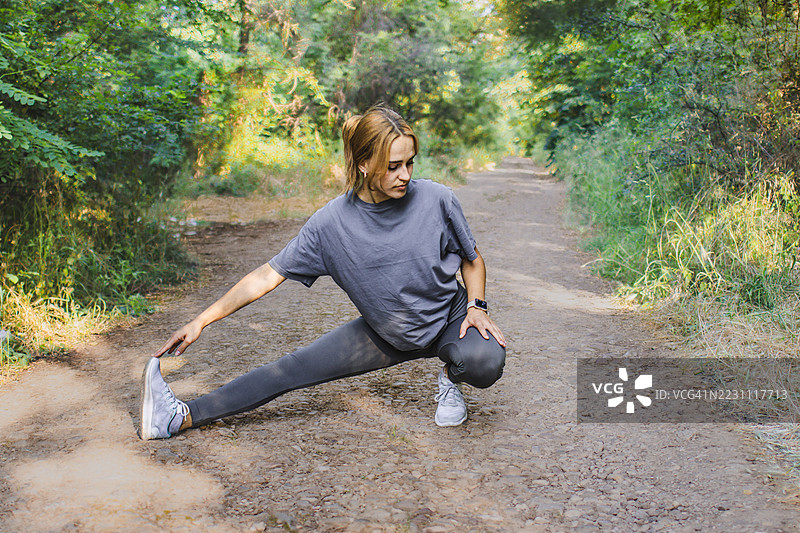美丽的年轻女性穿着运动服，在大自然中热身或拉伸。她在锻炼过程中平衡力量与柔韧性。积极的生活方式、心理健康与健身。图片素材