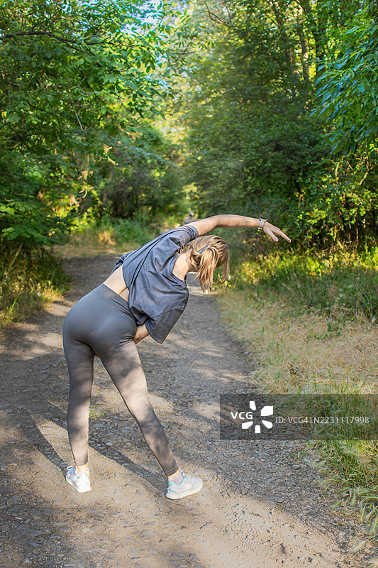 美丽的年轻女性穿着运动服，在大自然中热身或拉伸。她在锻炼过程中平衡力量与柔韧性。积极的生活方式、心理健康与健身。图片素材