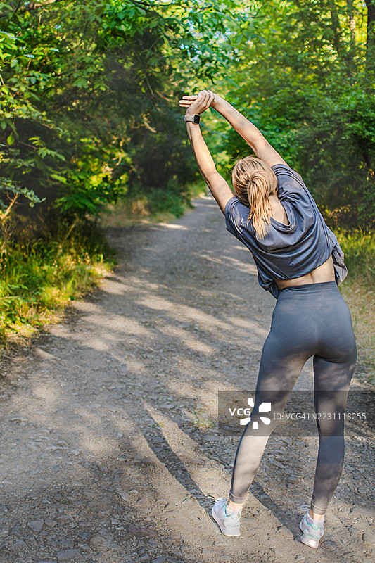 美丽的年轻女性穿着运动服，在大自然中热身或拉伸。她在锻炼过程中平衡力量与柔韧性。积极的生活方式、心理健康与健身。图片素材