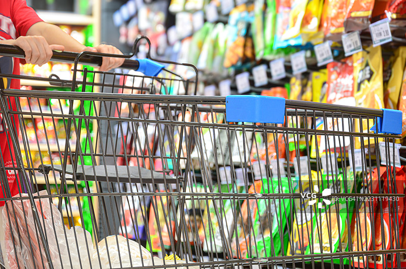 一位女性在超市推着购物车挑选商品。图片素材