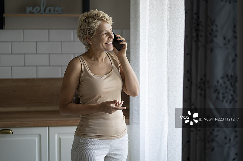 一位女性站在窗边，正在用手机通话。图片素材