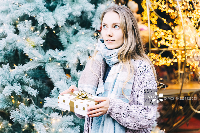 一位快乐的女性手持圣诞礼物盒，面朝一旁，脸上洋溢着喜悦的表情。图片素材