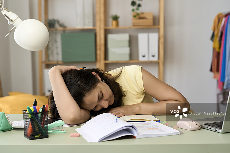 疲惫的年轻女性在家学习时趴在书本上睡着了图片素材