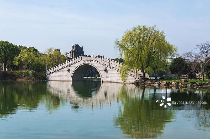 古老的石拱桥横跨宁静的湖泊，周围绿树成荫图片素材