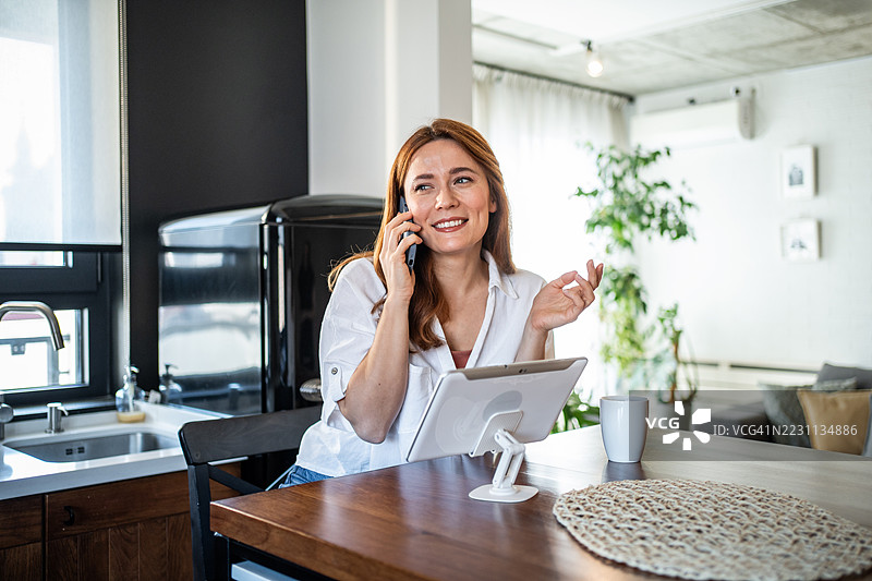 快乐的自由职业女性在家中一边打电话一边使用平板电脑工作图片素材