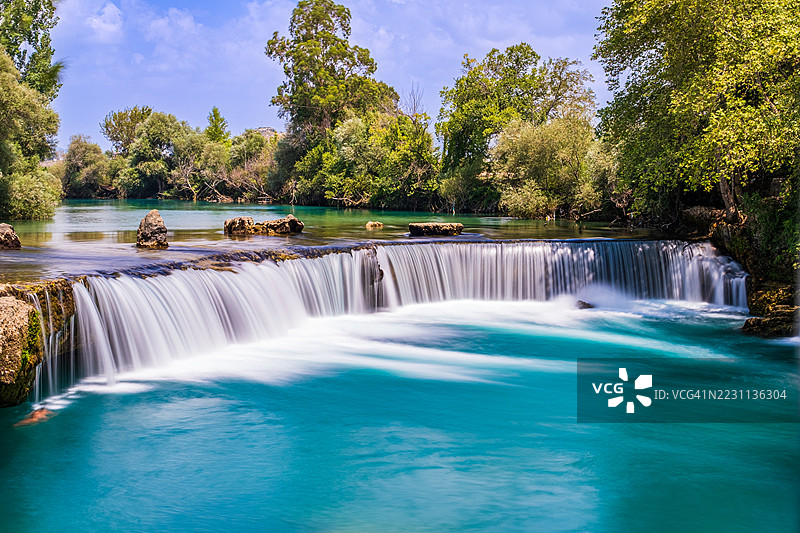 风景如画的瀑布流入碧绿色的河流，四周环绕着绿色森林图片素材