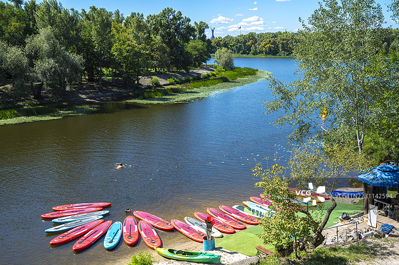 阳光明媚的夏日，河岸边五彩斑斓的划水板和皮划艇图片素材