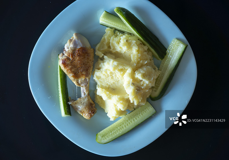 烤鸡腿配土豆泥和黄瓜片，摆放在浅蓝色盘子上图片素材
