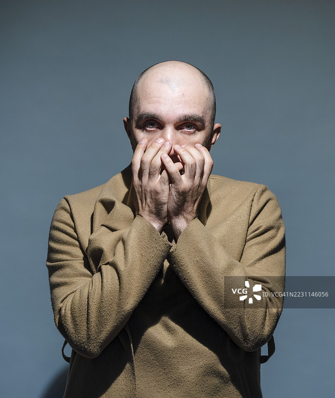 一位秃头男子用双手捂住嘴巴的戏剧性肖像图片素材