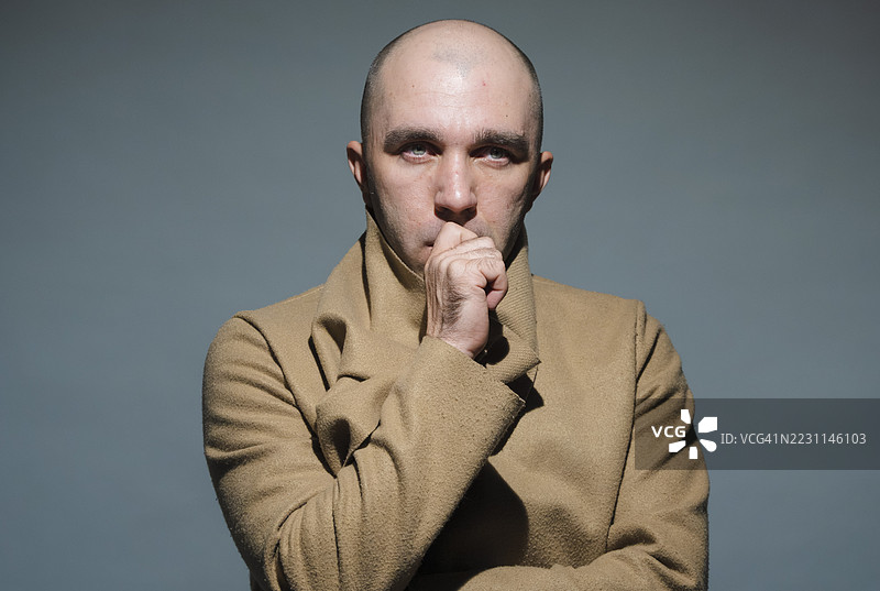 穿着米色外套的严肃男人，手托下巴，神情沉思。图片素材