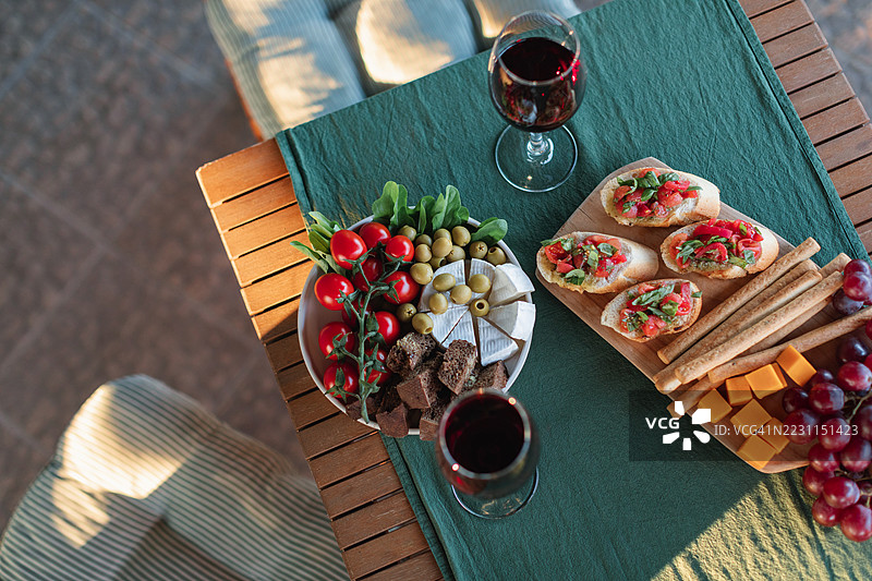 花园桌子上的番茄布鲁斯凯塔、面包棒、葡萄、樱桃番茄、卡门贝尔奶酪、黑面包、橄榄和红酒杯的俯视图图片素材