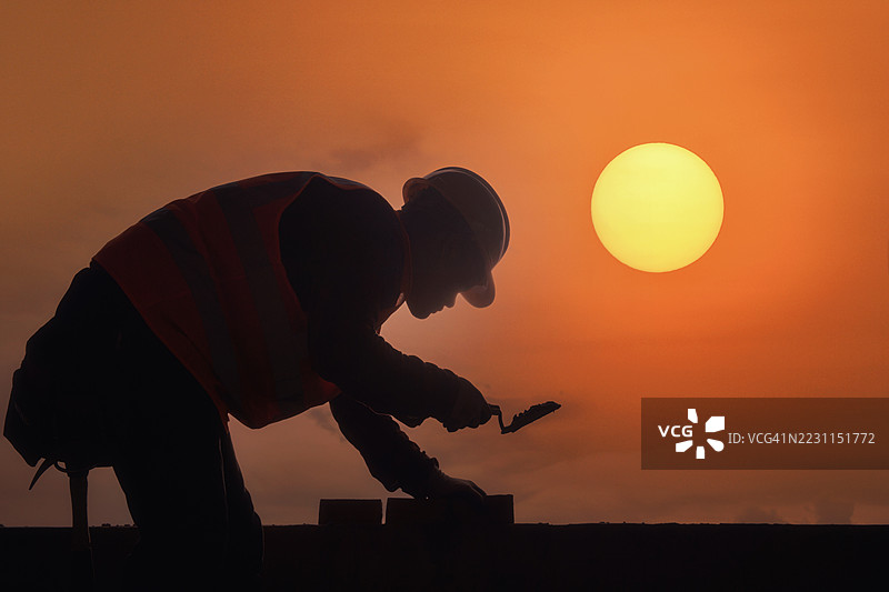 泰国日落时分，砖工在建筑工地上砌砖的侧面剪影图片素材