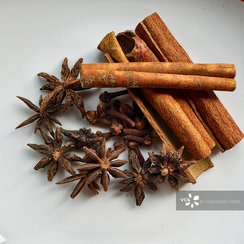 高角度视图的肉桂棒、八角和丁香放在白色盘子上图片素材
