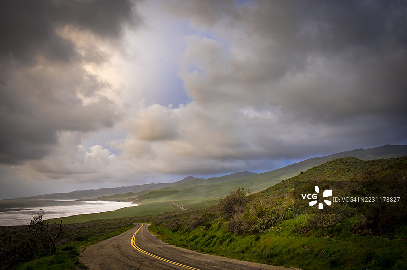 蜿蜒的海岸公路穿过绿色山丘，背景是戏剧性的天空，洛姆波克，美国图片素材