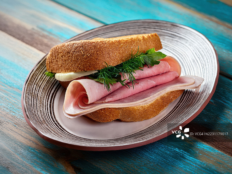美味的火腿三明治配新鲜香草，摆放在乡村风格的盘子上图片素材