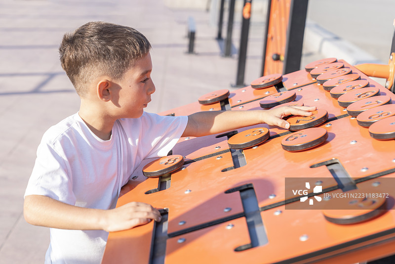 小男孩在玩教育面板。公共公园中的儿童教育户外玩具。公共公园中的精细运动游戏面板。数字排序面板。图片素材