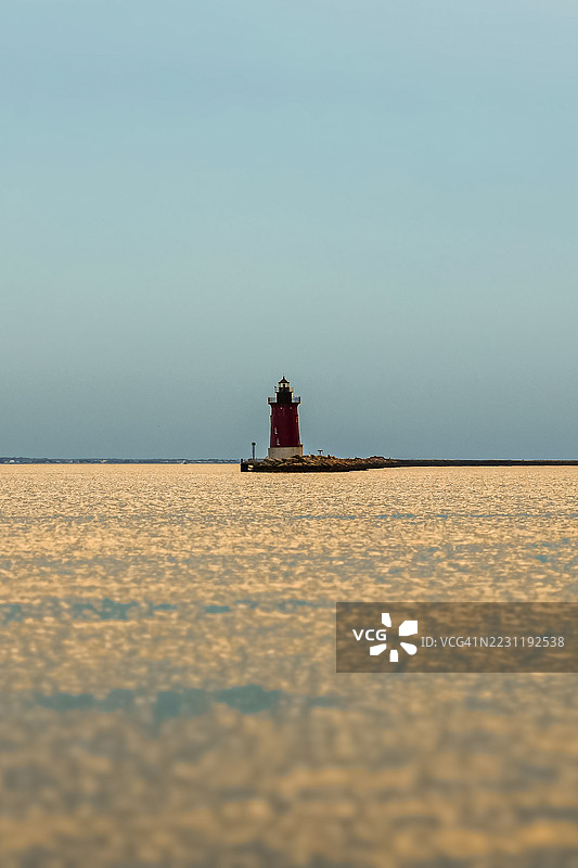 孤独的灯塔在日落时分的平静海面上，位于美国路易斯。图片素材